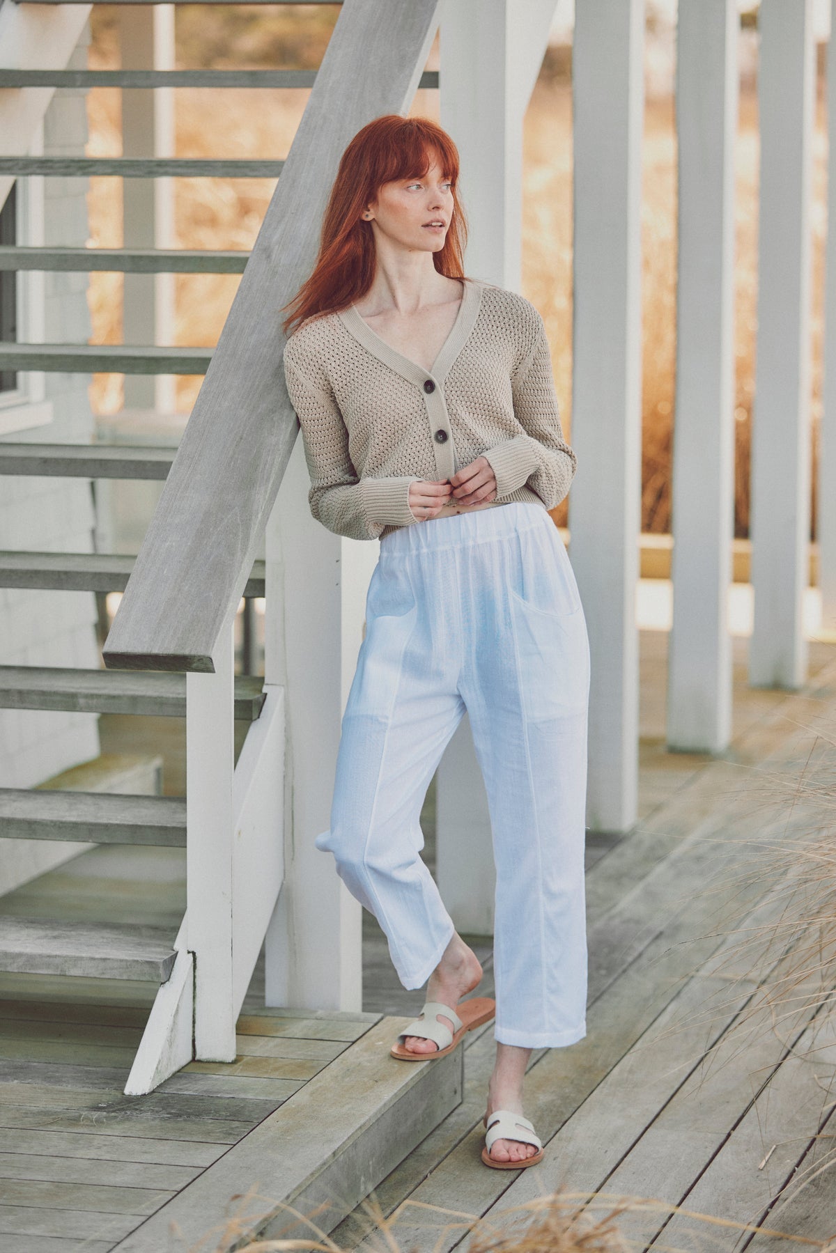 a model in a beige cardigan and white flowy pants