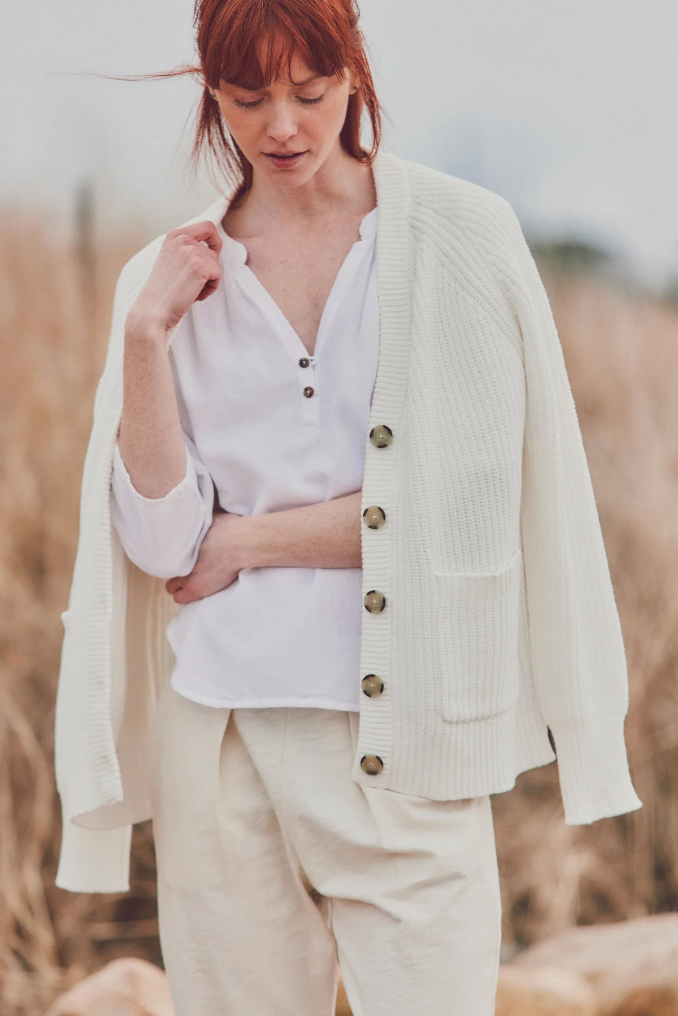 a model in a cream cardigan layered over a white henley top