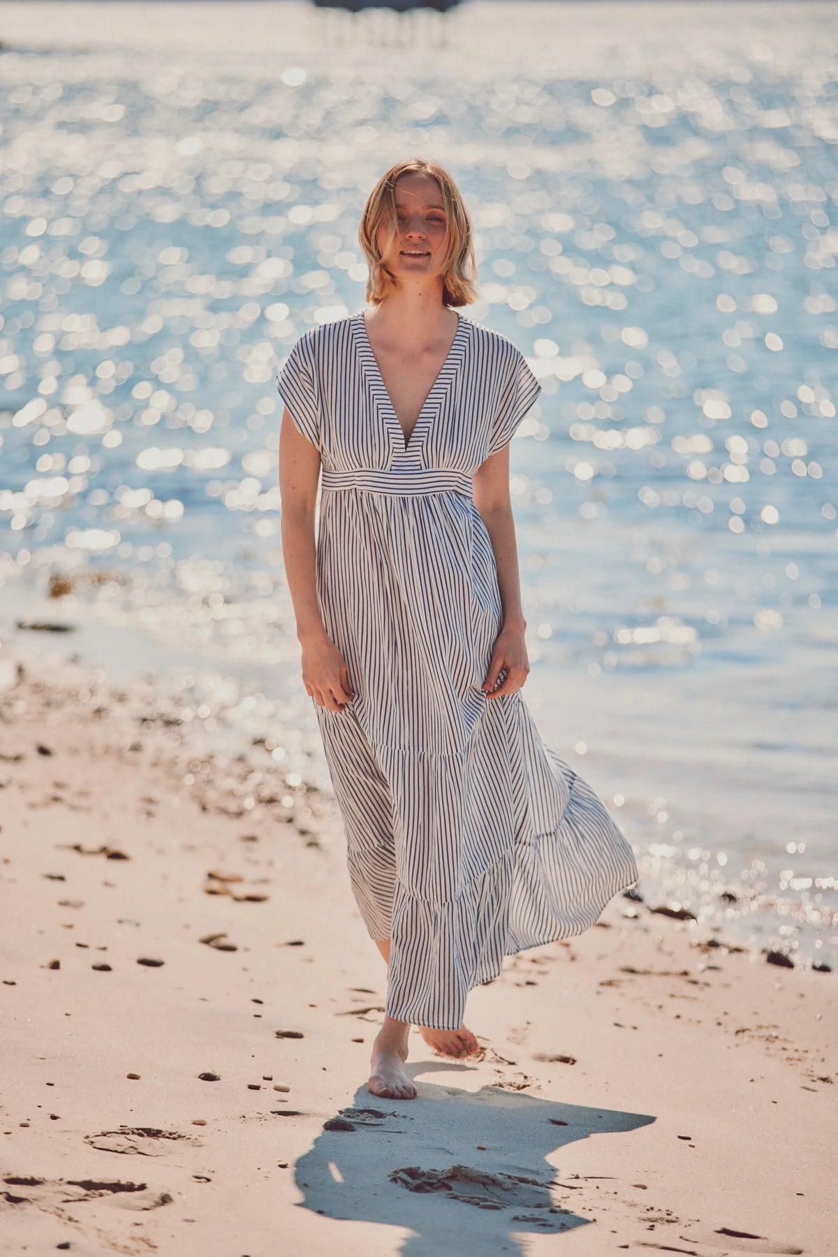 a model walking on the beach in a blue and white striped dress