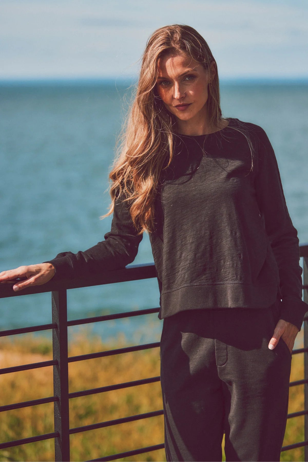 a model by the ocean in a black long-sleeve and pants