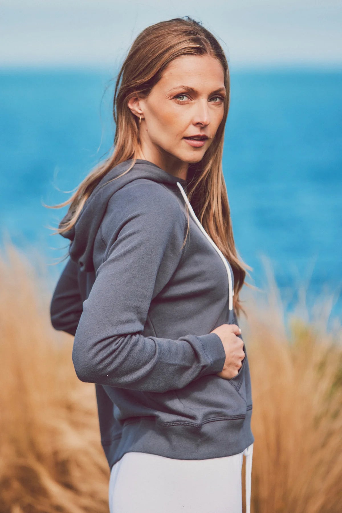 a model by the ocean in a blue hoodie