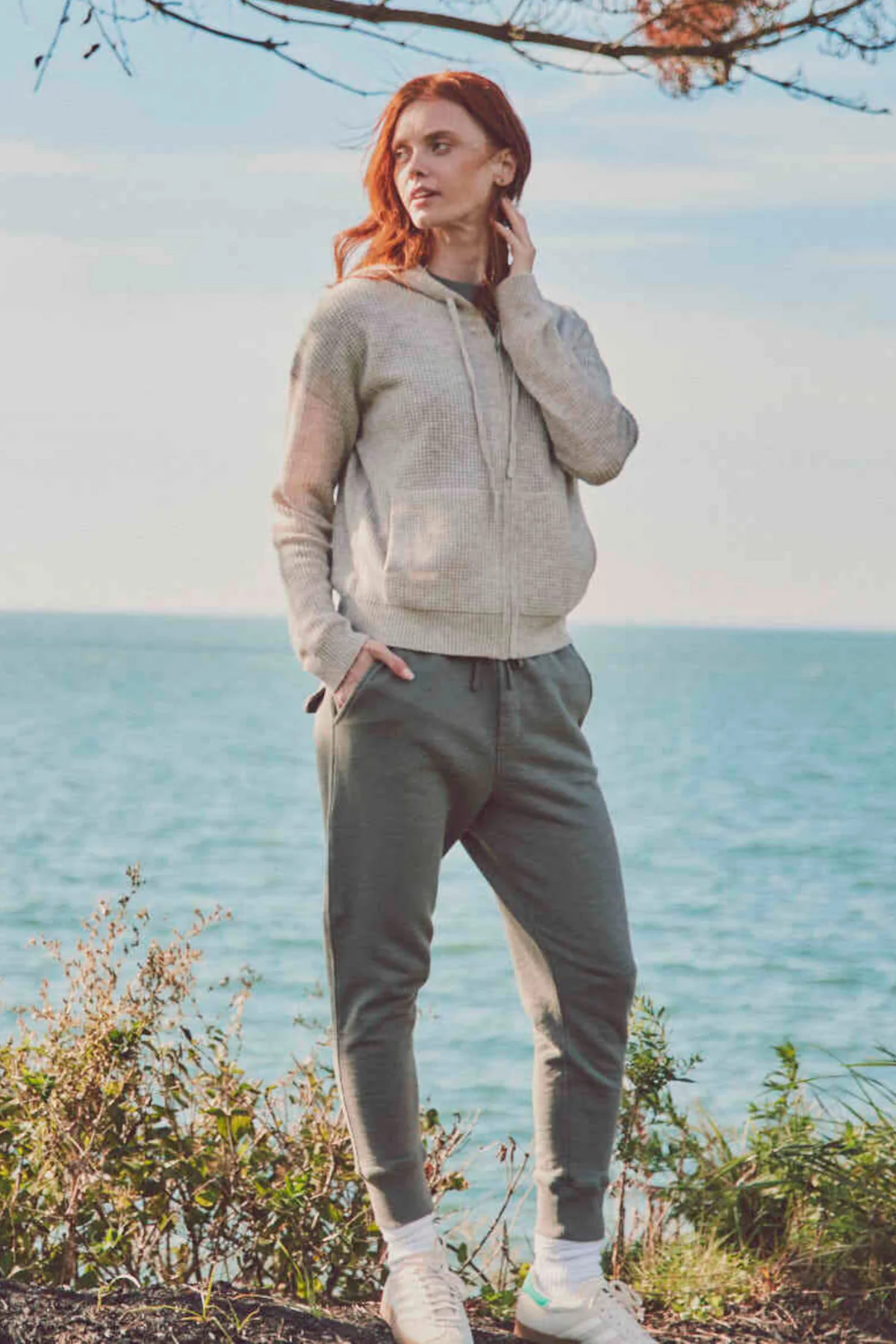 a model by the ocean in a cream hoodie