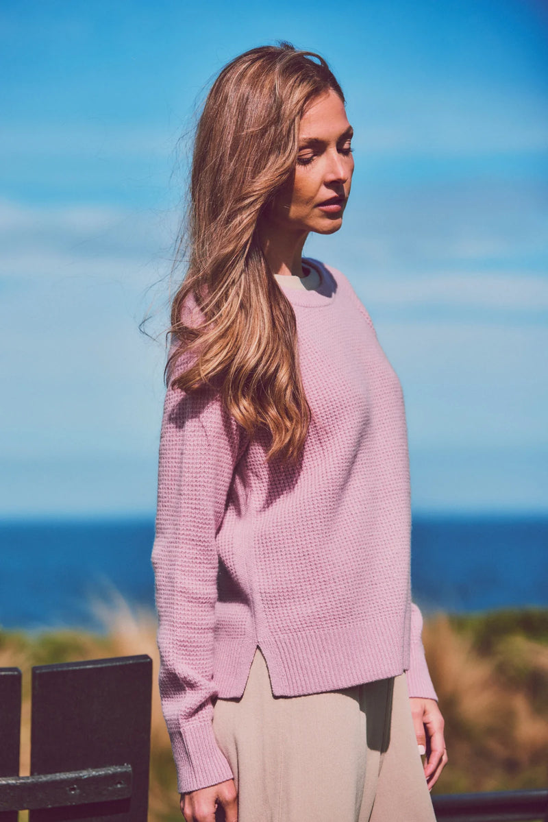 a model by the ocean in a pink knit sweater