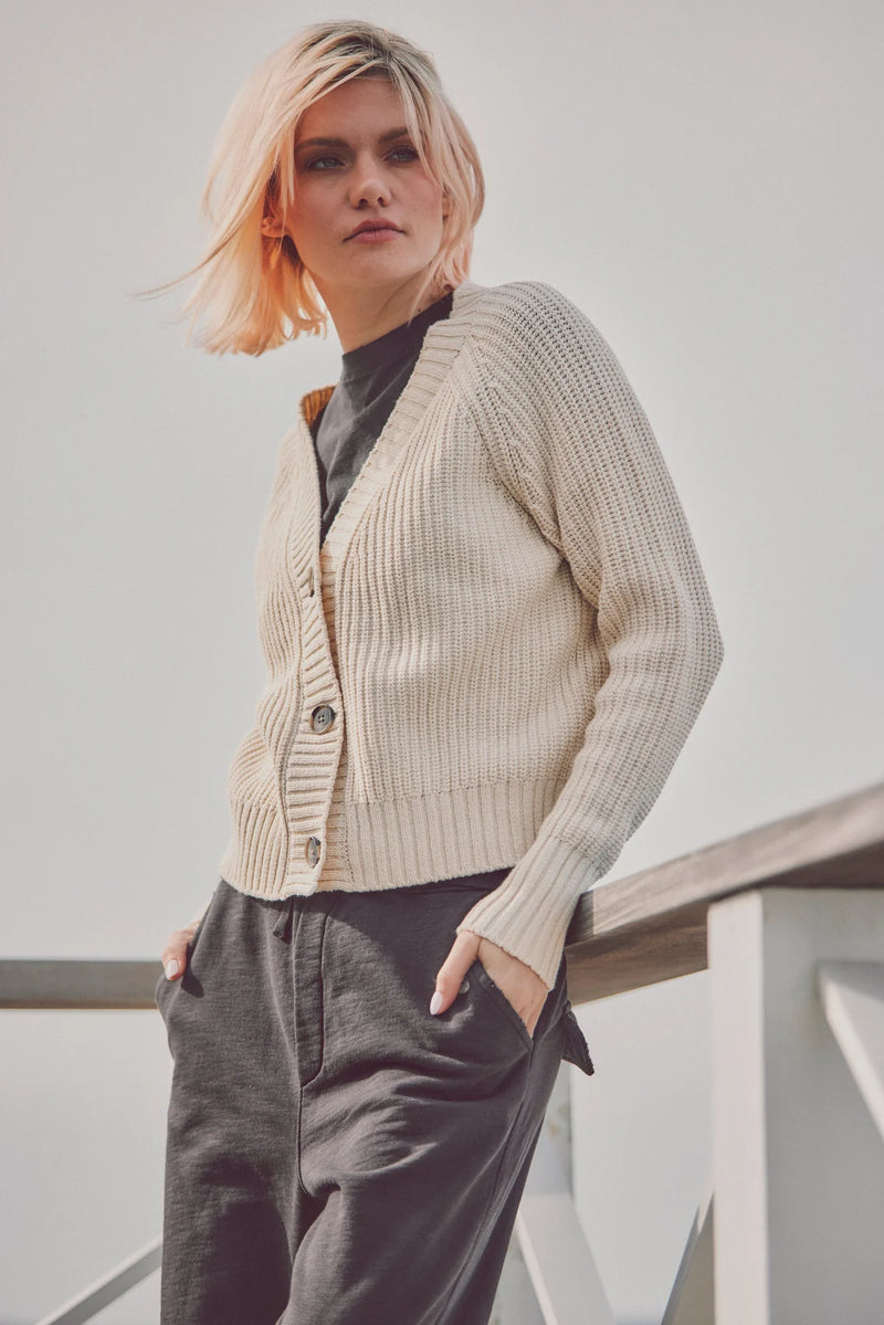 a model in a beige cardigan and gray pants