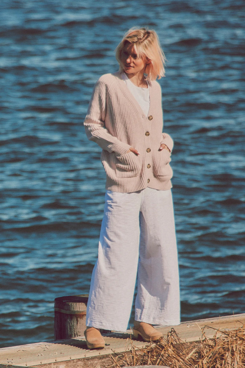 a model in a beige cardigan and white pants