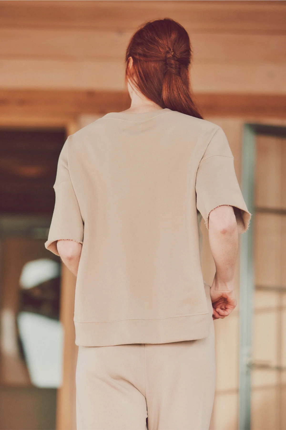 a model with red hair showing the back of beige joggers and a t-shirt