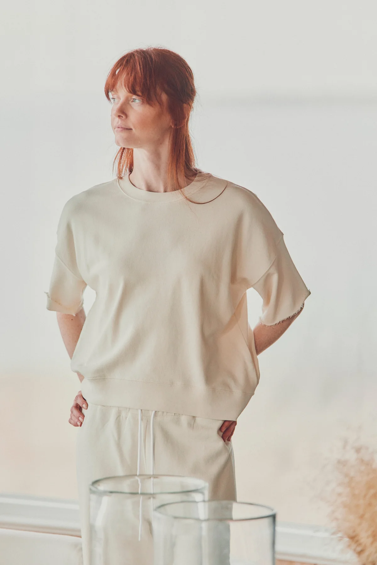 a model with red hair in a beige t-shirt in a white room