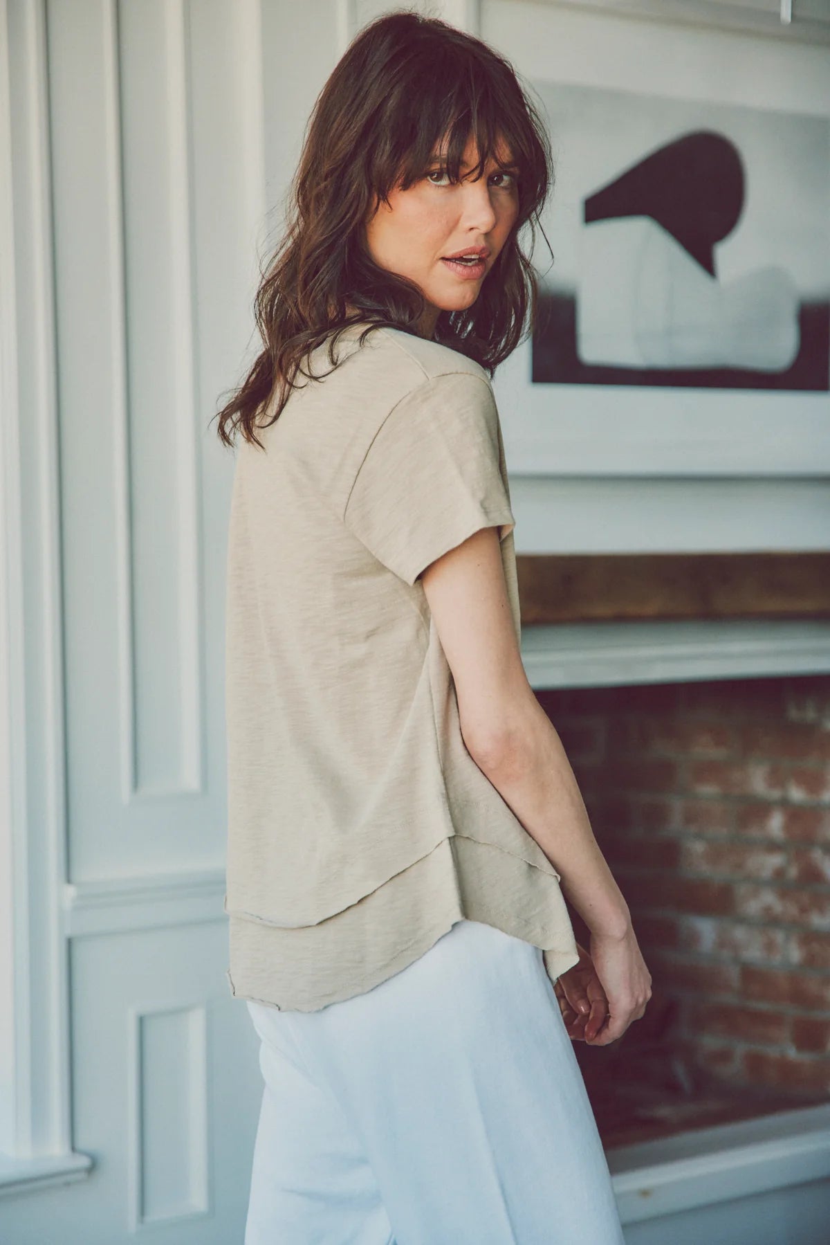 a model in a beige tee and white pants