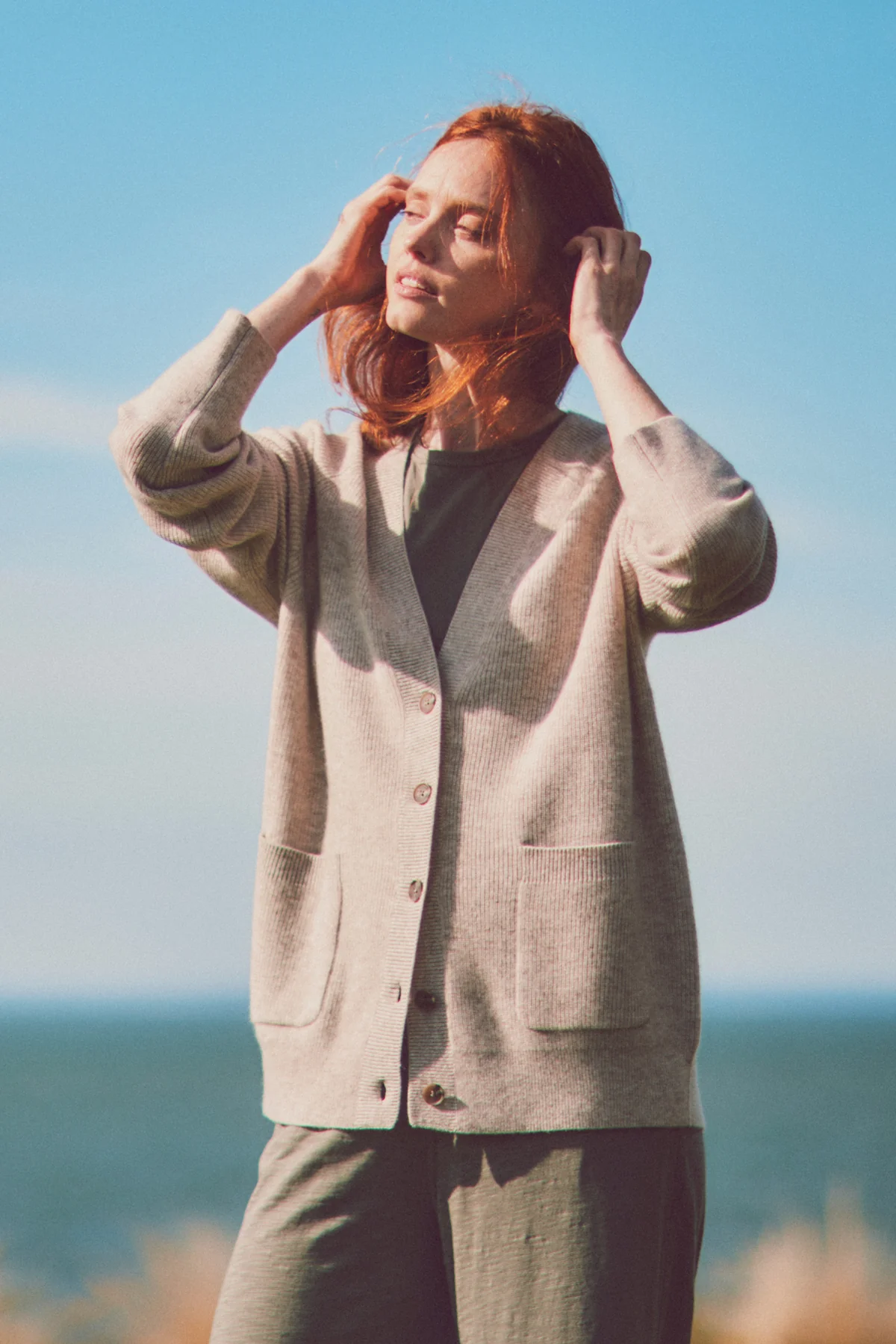 a model in a gray cardigan fixing her hair