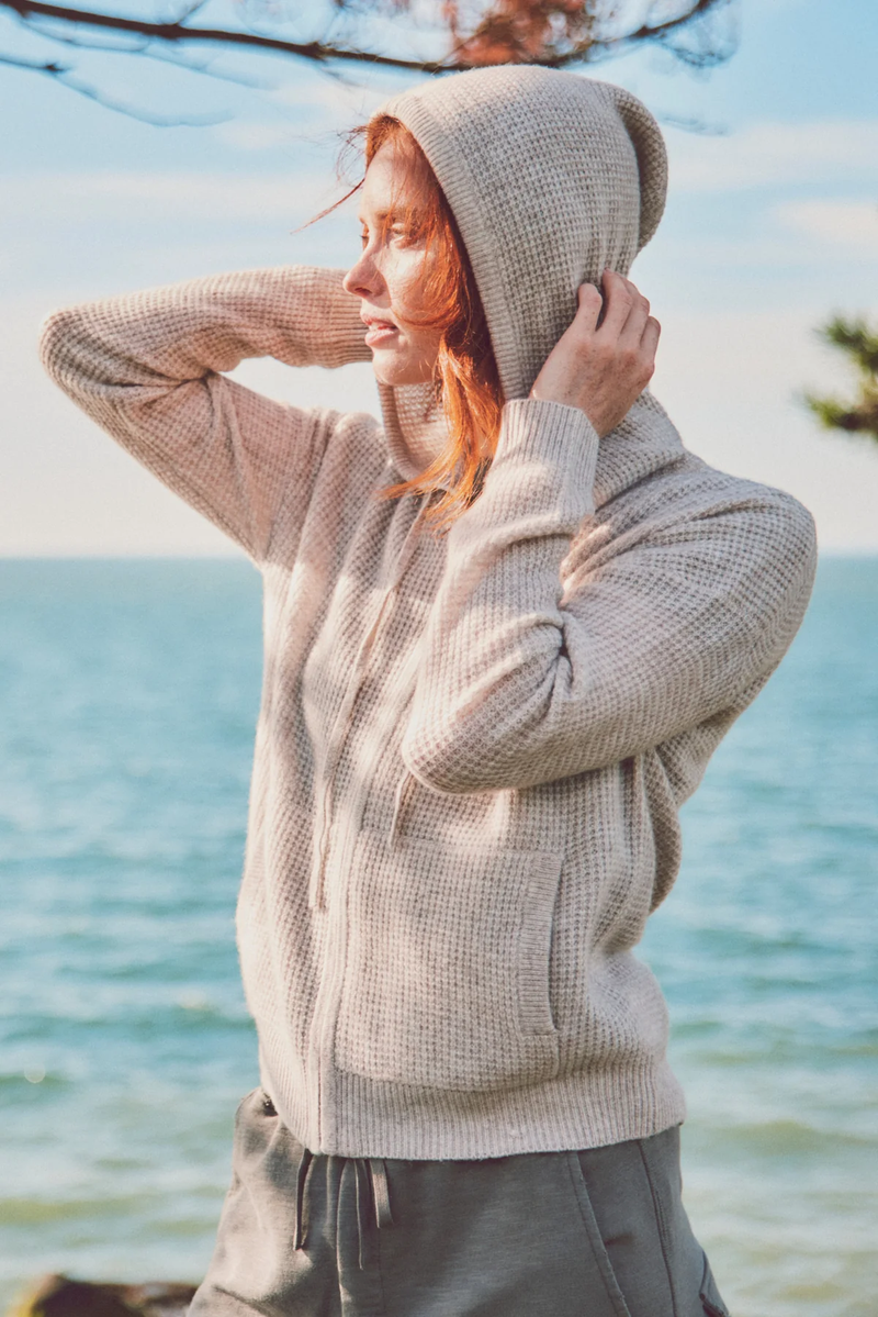 a model in a cream hoodie with hood up