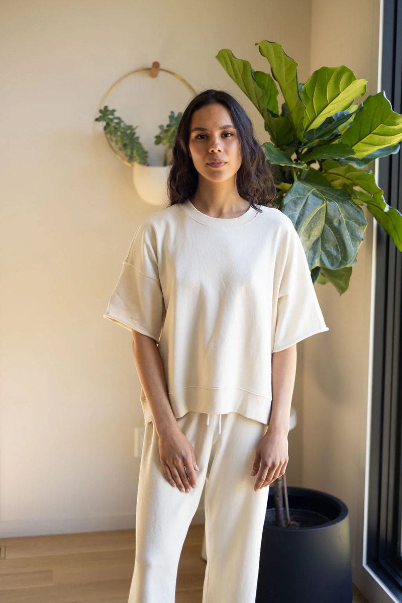 a model standing in front of a plant in a cream t-shirt and pants