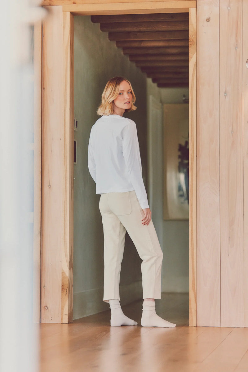 a model in a doorway in beige pants and a white top