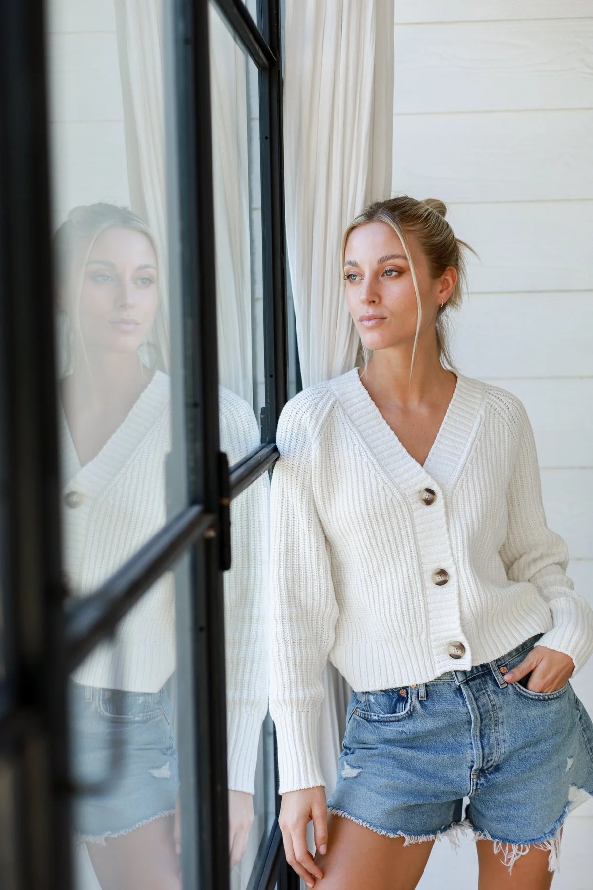 a model in a white cardigan and denim shorts