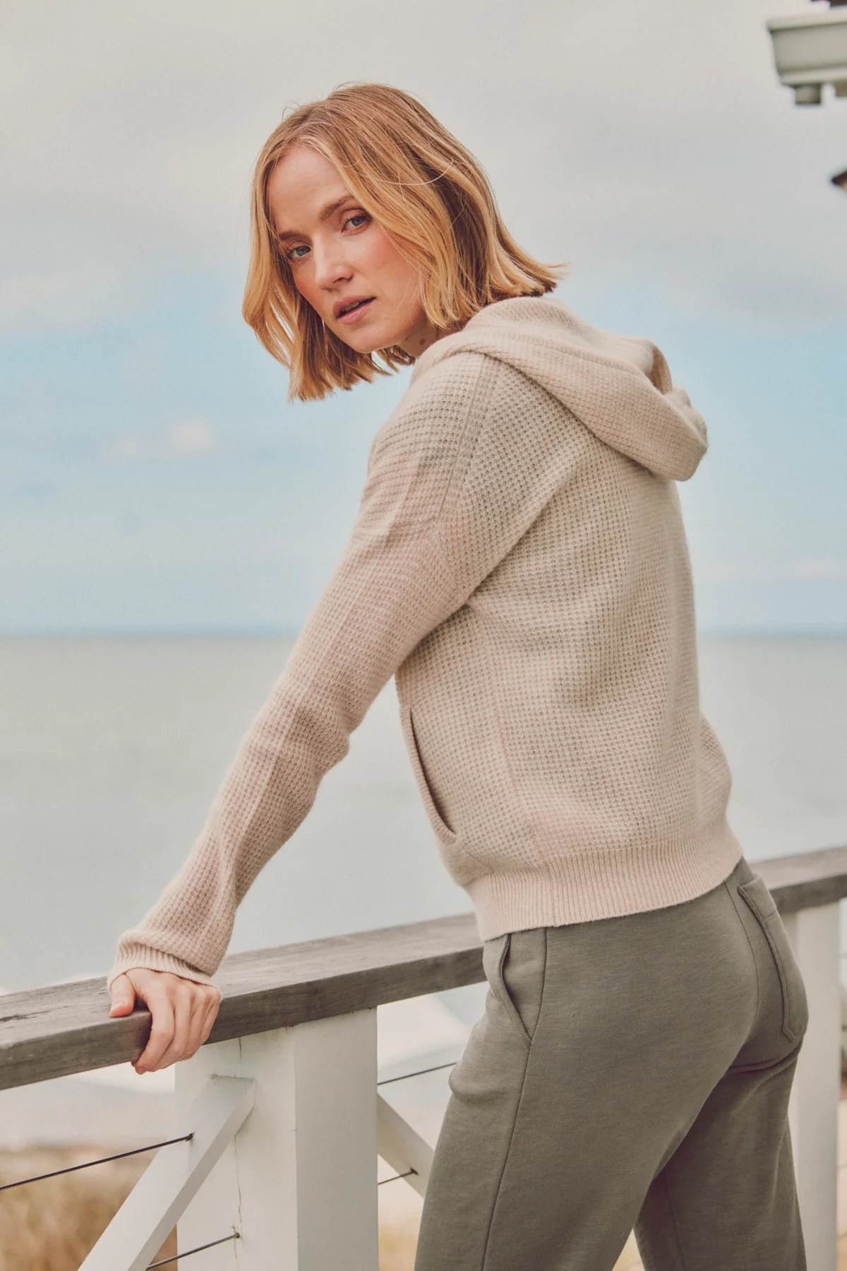 model leaning against railing in beige hoodie