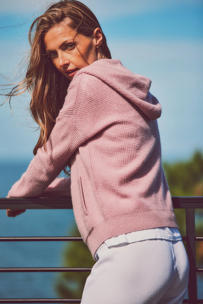 a model leaning on a railing in a pink hoodie