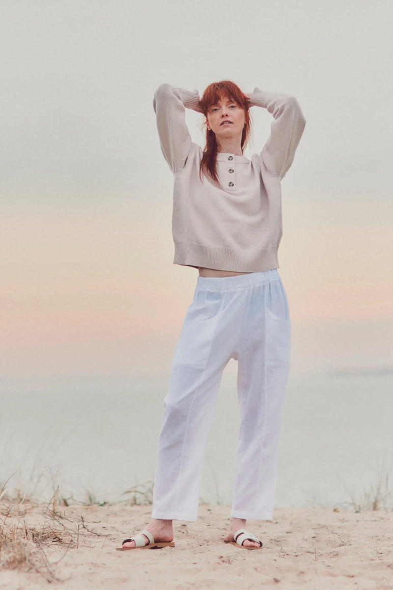 a model on the beach in white pants and a beige top