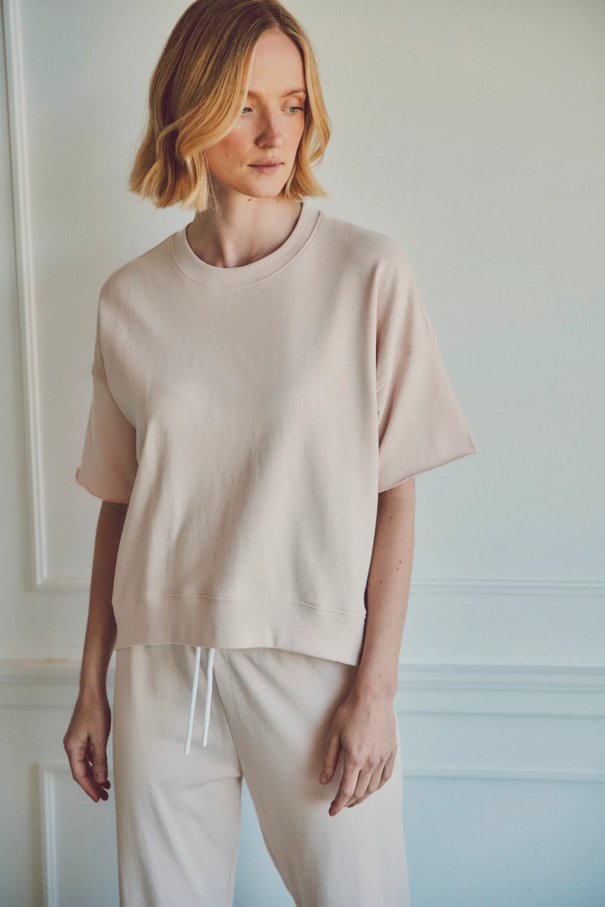 a model in front of a white wall in a beige shirt and pants