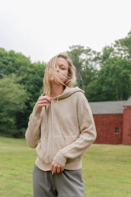 a model zipping up a beige hoodie