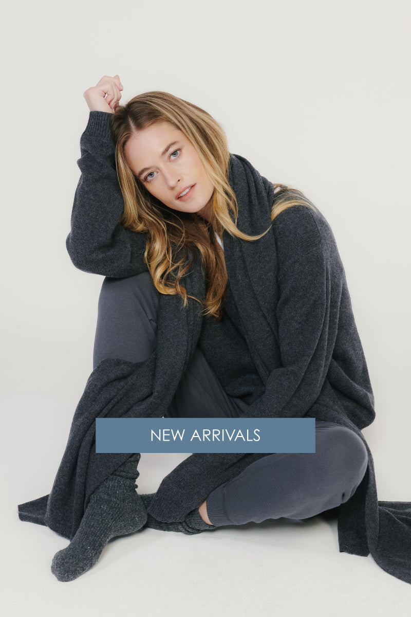 Model in charcoal cardigan wrap layered over joggers, seated in studio; text reads ‘New Arrivals.’